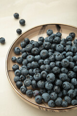 Beige ceramic bowl of fresh ripe blueberries on light background.