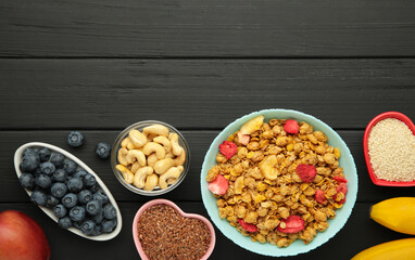 Granola with strawberries in a bowl with berries on black wooden background.