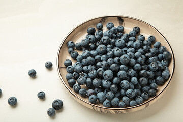 Beige ceramic bowl of fresh ripe blueberries on light background.
