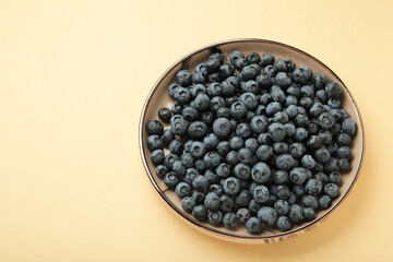 Beige ceramic bowl of fresh ripe blueberries on beige background.