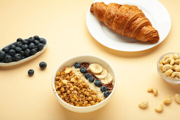 Beautiful morning breakfast with fresh croissants and granola with yoghurt on beige background. Tasty and healthy breakfast