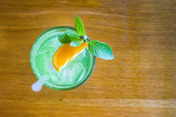 a glass glass of lemonade with ice, basil mint and a piece of orange on a wooden table. flatlay and copy space.