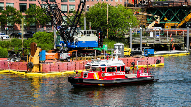 NORWALK, CT, USA - JUNE 15, 2024:  A red fireboat with the words City of Norwalk  next to a construction site with a large crane and other equipment