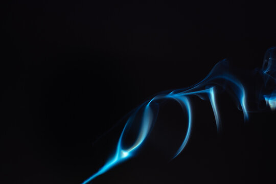 Blue smoke isolated on a black background. A thin curved line of smoke, steam from a burnt candle to overlay on your photos