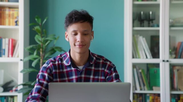 Modern biracial student learning remotely closeup. Stylish young adult guy working at home. Smiling freelancer watching webinar. Man using laptop computer in light space