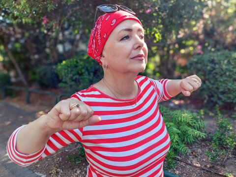 A mature woman, bald from chemotherapy, walks rapidly in the morning park, doing exercises as she goes, committing her free days to outdoor sports.
