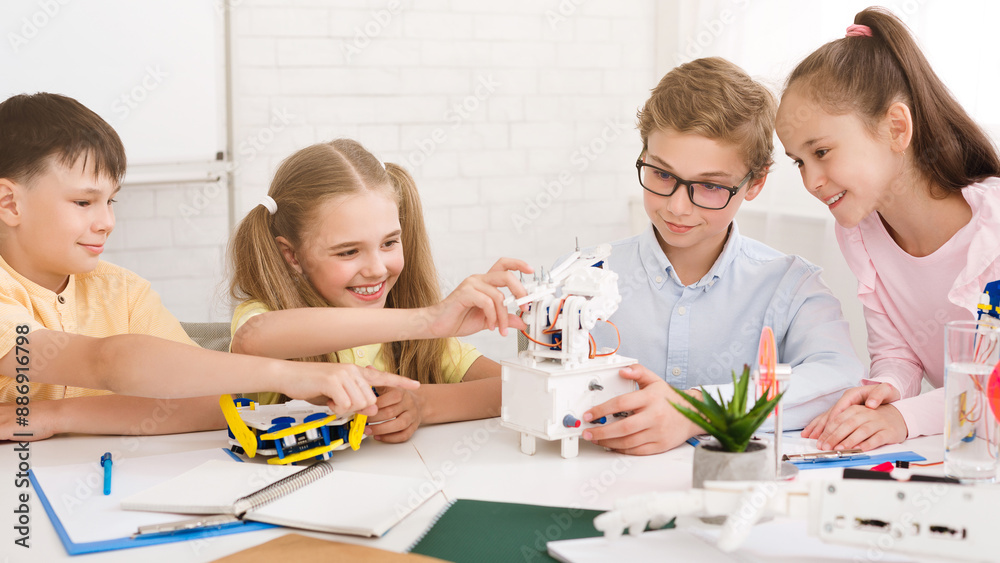 Fototapete A group of children, including two girls and two boys, are working on a robotics project in a classroom setting, smiling and appear to be enjoying themselves as they learn and build together.