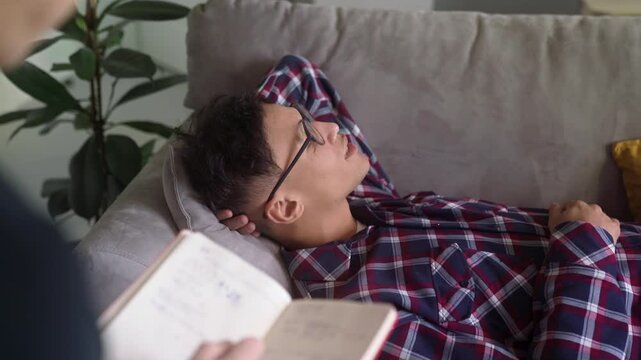 Therapy Session on Comfortable Sofa Biracial Young Man Patient Discussing Thoughts Feelings with Psychologist, Concept Mental Health, Emotional Support. Psychotherapist makes notes. One-on-one. 
