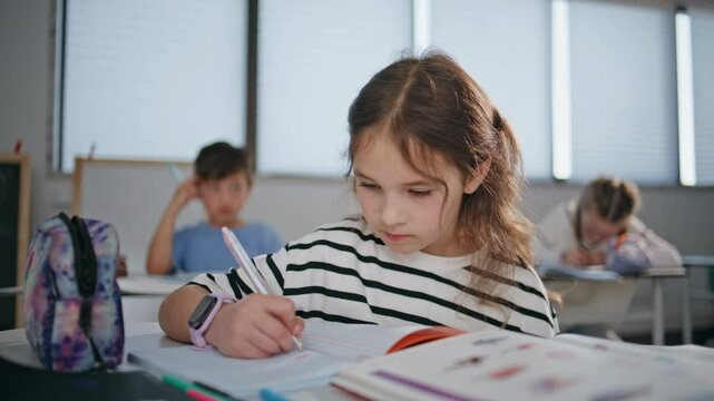 Attentive schoolgirl solving tests notebook in elementary school class closeup