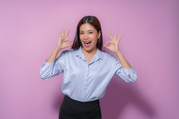 Young asian businesswoman in a blue shirt looks joyful, making an okay sign with both hands in her...