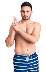 Fototapeta premium Young handsome man wearing swimwear holding symbolic gun with hand gesture, playing killing shooting weapons, angry face
