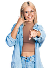 Beautiful young blonde woman wearing glasses smiling doing talking on the telephone gesture and...