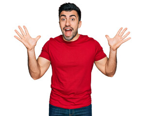 Hispanic man with beard wearing casual red t shirt celebrating crazy and amazed for success with arms raised and open eyes screaming excited. winner concept