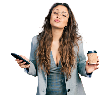 Young hispanic girl using smartphone and drinking a cup of coffee looking at the camera blowing a kiss being lovely and sexy. love expression.