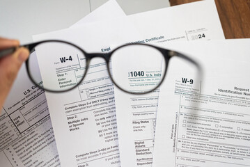Male hand holds glasses above different tax forms mandatory for taxpayers to report annual income...