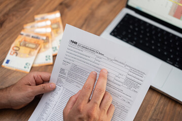 Naklejka premium Man company accountant holds tax form examining steps of filling blank correctly sitting at workplace with euro banknotes and laptop with digital table in office