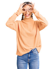 Fototapeta premium Beautiful caucasian woman with blonde hair wearing casual winter sweater doing ok gesture like binoculars sticking tongue out, eyes looking through fingers. crazy expression.