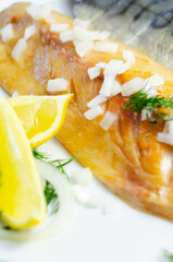 A smoked fish fillet with onions and lemon slices on top