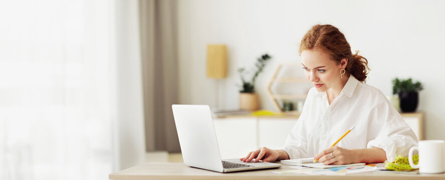 Writing Information. Young female student sitting at desk, using portable net-book, working at home, copy space