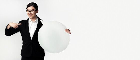A businesswoman in a black suit and white shirt is holding a large white circle and pointing to it.