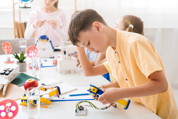 A young boy is focused on assembling a robot during a robotics class. He is sitting at a table with...