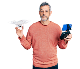 Middle age hispanic man with grey hair using drone with remote control relaxed with serious expression on face. simple and natural looking at the camera.