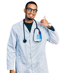 Fototapeta premium Young african american man wearing doctor uniform and stethoscope smiling doing phone gesture with hand and fingers like talking on the telephone. communicating concepts.