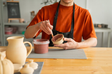 Close-up of a potter's hands with a brush painting ceramic dishes. 