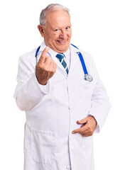 Senior handsome grey-haired man wearing doctor coat and stethoscope beckoning come here gesture with hand inviting welcoming happy and smiling