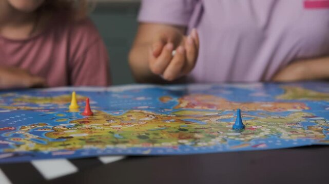 Close-up of mother rolling dice while playing with young daughter a board game indoors, slow motion. Enjoying spending time together on the weekend