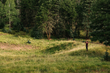 A man in a camouflage jacket stands looking through binoculars in a clearing while hunting for Elk in the Valles Caldera National Preserve, New Mexico