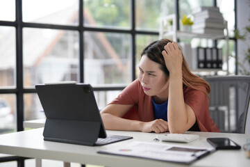 Young businesswoman is feeling stressed while working on a digital tablet in the office. She is having a problem with her work and is feeling overwhelmed