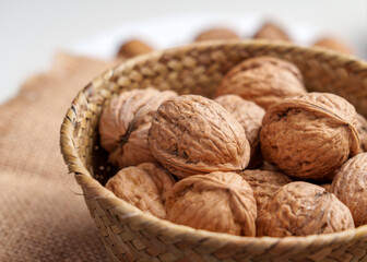 Whole walnuts in wooden rattan bowl, their shells showing intricate patterns and textures. They are ready to be cracked open, revealing the delicious nut inside. Close up