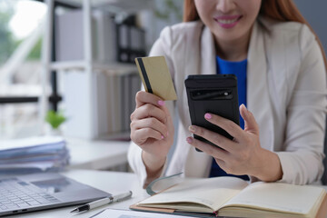 Fototapeta premium Businesswoman happily shops online with a credit card and smartphone at her office desk, showcasing modern e commerce convenience