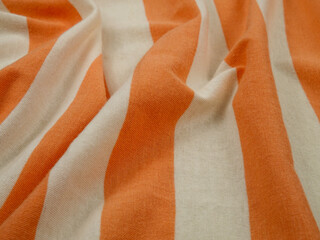 White thin arbitrarily folded fabric with wide orange stripes, background
