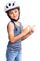 Little cute boy kid wearing bike helmet smiling and looking at the camera pointing with two hands and fingers to the side.