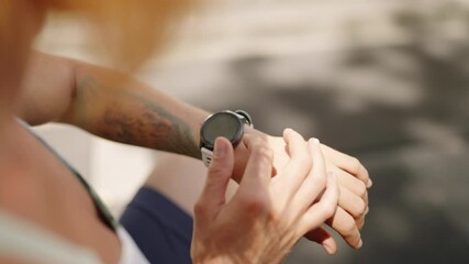 Redhead athlete checks smart watch after training in outdoor gym. Pro sportswoman monitors heart rate, calories burned, in tropical setting. Fitness session, health stats tracking in sunlight. Slowmo - Powered by Adobe