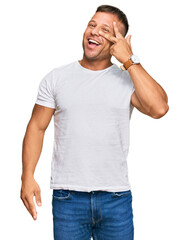 Handsome muscle man wearing casual white tshirt doing peace symbol with fingers over face, smiling cheerful showing victory