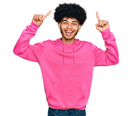 Young african american man with afro hair wearing casual pink sweatshirt smiling amazed and surprised and pointing up with fingers and raised arms.