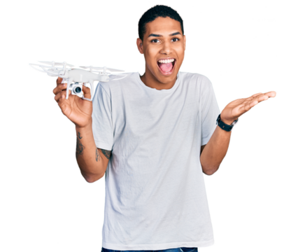 Young hispanic man holding drone celebrating achievement with happy smile and winner expression with raised hand