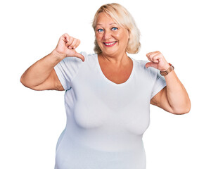 Middle age blonde woman wearing casual white t shirt looking confident with smile on face, pointing oneself with fingers proud and happy.