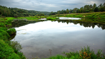 The tranquil nature setting showcases a calm pond surrounded by verdant vegetation