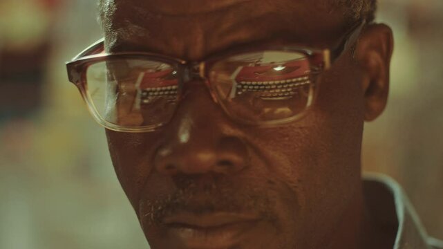 Close-up view of face of senior African American investigator typing on retro manual typewriter reflected in his eyeglasses