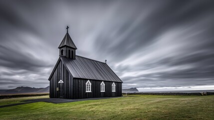 Fototapeta premium A black church stands on a grassy hill with a paved road leading into the distance. The sky is overcast with dark clouds