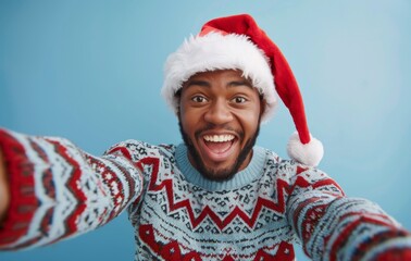 Happy man wearing Christmas sweater and Santa hat taking selfie against blue background