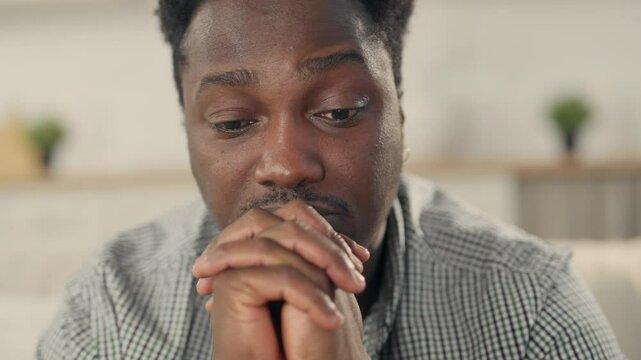 Stressed and frustrated black man sitting alone at home, closeup portrait. Unhappy young adult African American person feeling sad thinking about psychological problems, suffering from loneliness