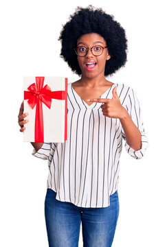 Young african american woman holding gift smiling happy pointing with hand and finger