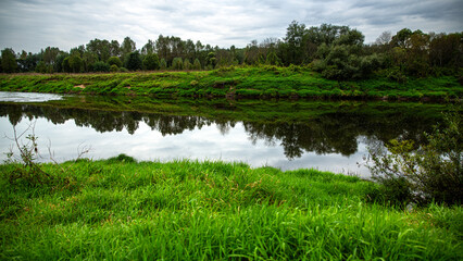 Fototapeta premium Enjoy a tranquil river landscape surrounded by lush greenery, reflected in calm waters