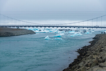 Stranded Iceberg broken off from glacier field floating around in Jokulsarlon in Iceland, going under a suspension bridge