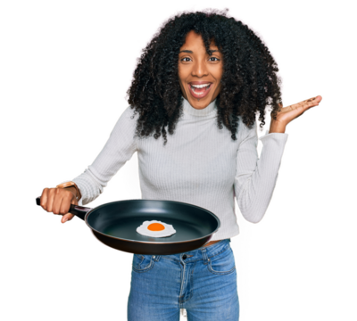 Young african american girl holding skillet with fried egg celebrating victory with happy smile and winner expression with raised hands